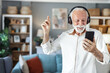© Jelena Stanojkovic - Middle aged man joyfully dancing indoors wearing headphones holding a smartphone enjoying music and expressing happiness in a modern home.