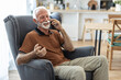 © Jelena Stanojkovic - Shot of an elderly man on a call using his cellphone on the sofa at home. Elderly guy enjoys online chatting, spends time in social networks, using phone and smiles.