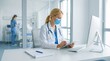 © Muchamad Musa - Female physician wearing a protective face mask works diligently on a tablet while sitting at a clean desk inside a modern, sterile hospital.