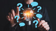 © MdAyub - Person touching a glowing light bulb surrounded by question marks and speech bubbles, symbolizing ideas and solutions