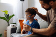 © kleberpicui - Father assisting young child during nebulizer therapy at home, showing parental care, pediatric respiratory treatment and emotional family support.
