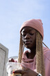© wavebreak3 - African American teen holding clear container at plaza, pink beanie, hoodie, showing red nails