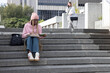 © wavebreak3 - Two women sitting on concrete steps at campus, one pink-hoodie reading notes, other using phone