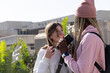 © wavebreak3 - Diverse female friends standing on campus, holding smartphone with headphones and backpack