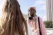 © wavebreak3 - Diverse female friends standing and talking in urban plaza wearing pink hoodie, beanie, headphones