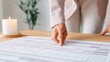 © afridwi - Womans hand points at document on desk close up with candle and plant background