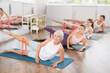 © JackF - Elderly woman lies on mat and performs stretching exercises with resistance bands in a group pilates class