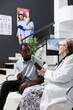 © DC Studio - Doctor in lab coat explains medication bottles to black man during consultation in clinic waiting room. Physician and patient discuss treatment options, dosage and medical advice in hospital lobby.
