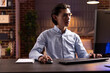 © DC Studio - Asian man works remotely during evening hours, researching strategies and improving plans for small business. Freelancer concentrates on pc screen, typing and reviewing marketing data in home office.