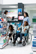 © DC Studio - Asian woman stands with friend in wheelchair as pharmacist selects rehabilitation medication from shelf. Modern pharmacy illustrates inclusive healthcare, professional guidance and supportive service.