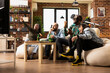 © DC Studio - Cheerful group of friends enjoys weekend VR gaming in modern apartment. Diverse people engage in virtual reality with drinks and snacks, bonding in cozy living room during fun leisure time.