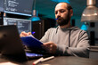 © DC Studio - Focused programmer flips through paperwork, cross checking information on laptop. Adult male developer holds pen and carefully reviews data on clipboard, ensuring accuracy within technical interface.