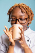 © DC Studio - Closeup of professional cook sipping coffee from disposable mug with eyes closed, enjoying caffeine aroma. Female restaurant worker takes calm moment to relax and recharge against blue background.
