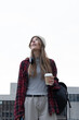 © wavebreak3 - Female commuter standing in front of concrete building holding paper coffee cup and wearing beanie
