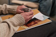 © pressmaster - Caucasian middle aged woman holding patterned fabric in hands while sitting with printed materials on lap during therapy session, close up showing focus on hands and papers