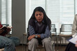 © pressmaster - Hispanic woman sitting with eyes closed and distressed expression during group therapy session, surrounded by other people, hands clasped together, participating in discussion