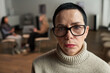 © pressmaster - Portrait of sad middle aged Caucasian woman with short hair and glasses looking into camera, sitting in foreground while two women having conversation in blurred background