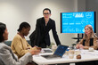 © pressmaster - Caucasian middle aged woman standing at conference table, leading business meeting with diverse group of women discussing charts and data on digital screen in office
