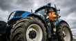 © Gayan - Adult white man construction worker in high-visibility orange safety vest and reflective pants standing on a large tractor outdoors under a cloudy sky, holding a yellow hard hat and wearing earmuffs.