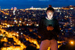 © Westend61 - Young woman using cell phone at night above the city, Barcelona, Spain