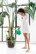 © Daniel - Woman watering large houseplant for plant care concept