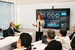© artitwpd - Executives in a boardroom watch a presenter explain performance dashboards on a large screen, discussing metrics and strategy during a corporate meeting.