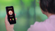 © Piya W. - Anxious elder woman holding smartphone looking at screen showing phone scam warning call alert against green nature blur background