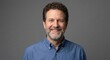 © Sophia - Smiling middle-aged man with a beard and curly hair looks directly at the camera, exuding confidence and approachability on a solid gray background