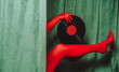 © VISTA by Westend61 - Red gloved hand and leg with vinyl record and high heel by green velvet curtain