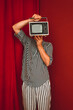 © VISTA by Westend61 - Person in striped clothing holding retro TV in front of face in red room