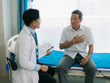 © ArLawKa - An Asian male doctor and an elderly patient are talking on a bed in a hospital room.