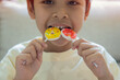 © Kunlathida - Happy Asian little boy eating two big sweet lollypop candy at home