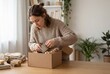 © DDA - Young woman unpacking items from a cardboard box at home