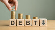 © Gambar - Reducing Debt: Hand adding coin to decreasing coin stacks on blocks spelling DEBT