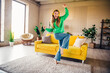 © deagreez - Young woman in a green sweatshirt cheerfully dancing in a vibrant loft style living room during a sunny day indoors