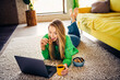 © deagreez - Relaxing young woman enjoying leisure time at home with laptop and snacks in cozy and stylish living space