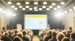 © Hassan - Blurred image capturing the essence of a large conference or seminar event with an audience focused on a bright projection screen and a speaker presenting to the attendees.