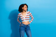 © deagreez - Young stylish woman in striped cardigan and jeans poses happily against a bright blue backdrop