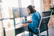 © deagreez - Businesswoman coding at a modern loft office with dual monitors and a focused freelancer at workstation