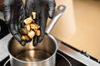 © pavel siamionov - A chef in black gloves adds pieces of fried meat and mushrooms to a saucepan on an induction stove.