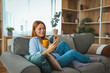 © Dragana Gordic - Smiling Woman Relaxing on Couch at Home Using Smartphone and Holding a Coffee Mug