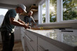 © Milos - Two men skillfully installing a countertop in a sunlit kitchen, showcasing collaboration and craftsmanship in home improvement and renovation projects.