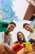© Xavier Lorenzo - Vertical shot of young group of people using phones devices standing together in circle outdoors. Millennial friends addicted to social media app, betting or playing video game on platform online.