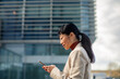 © Marko Geber - Businesswoman using smartphone outside modern office building