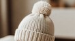 © TokoRezeki - A close-up shot of a knitted hat with a pom-pom on top sits on a table indoors.