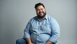 © Vadym - Plus size man in blue shirt laughs heartily. He wears denim jeans and sits against a plain grey background. His expression shows pure joy and confidence. Man looks happy, friendly and approachable.
