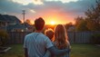 © Pete - Family watches sunset in backyard. Parents hug son, contemplating future and hope. Warm golden hour light illuminates home and outdoor space. Togetherness shown.