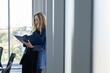 © eakgrungenerd - Confident businesswoman reviewing documents in modern office, professional manager analyzing reports near window, corporate leadership, focused planning and executive decision making concept