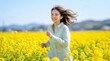 © WOWSTYLE - 菜の花畑の中を元気よく走る笑顔の女性