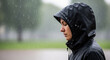 © Imaginarium_photos - Woman wearing a black rain jacket stands with her eyes closed outdoors while heavy rain falls around her.